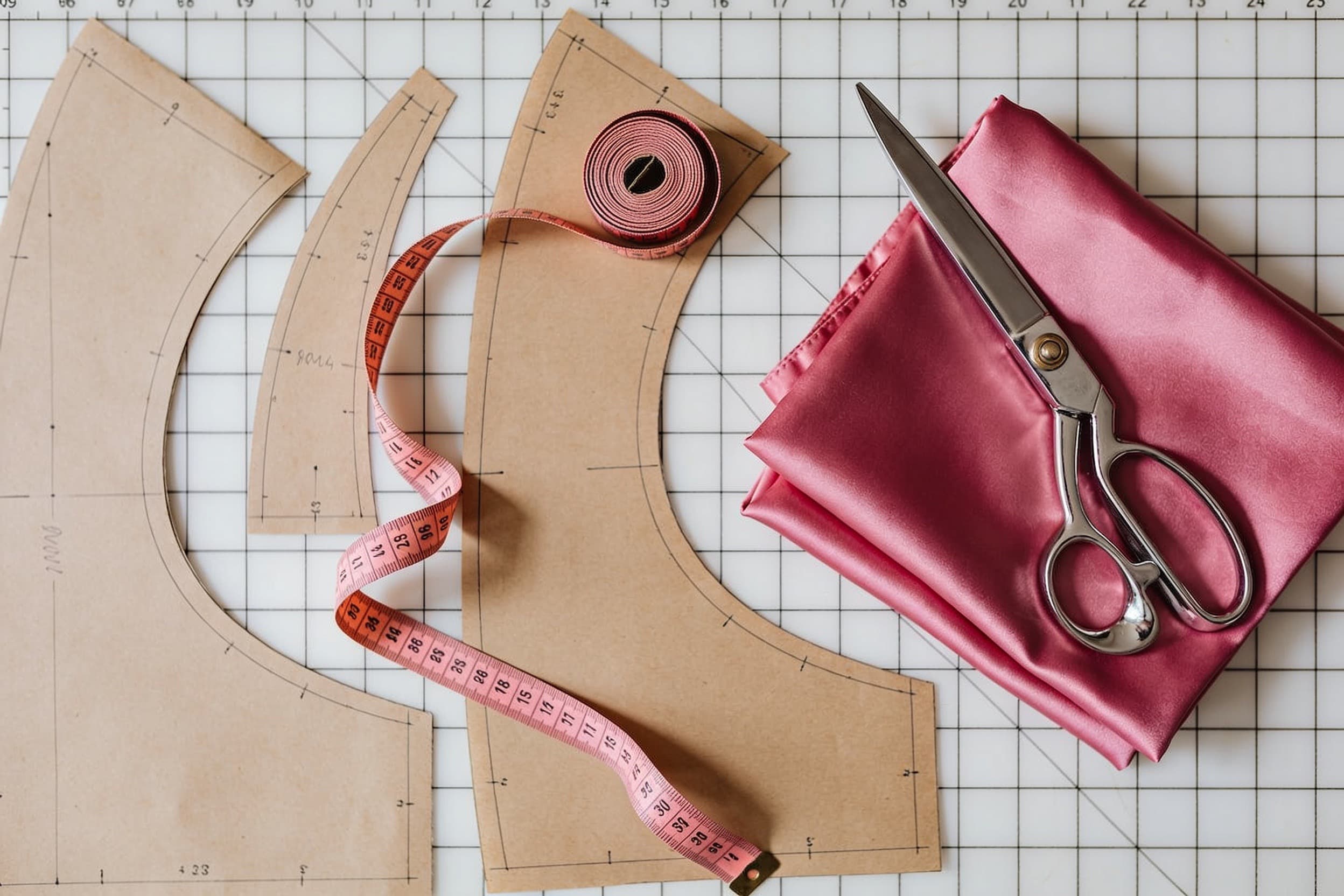 Pattern pieces, a pink tape measure and shears on pink satin, laid out on a cutting mat